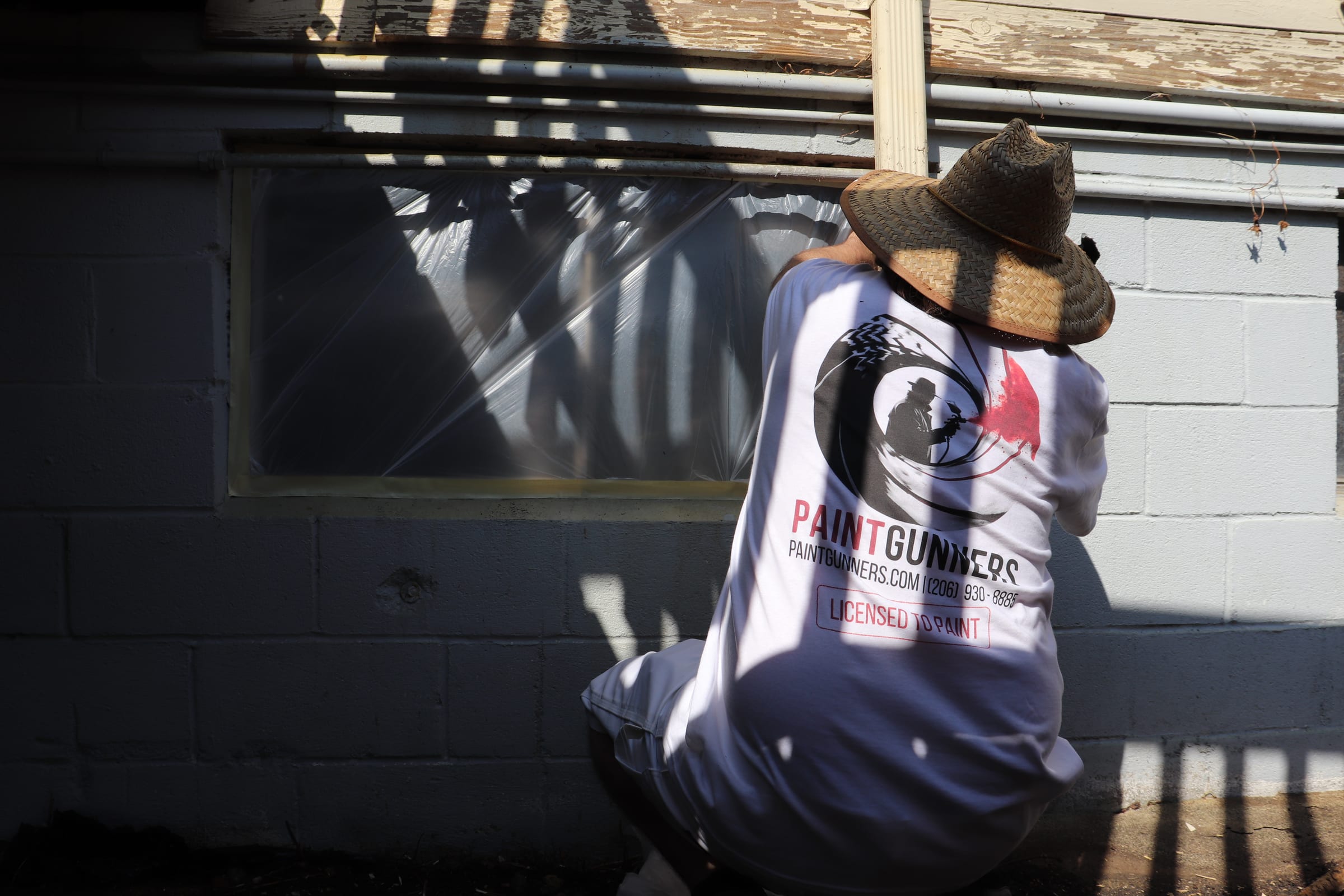 Painter in a Paint Gunners shirt masking off a window on a concrete block wall
