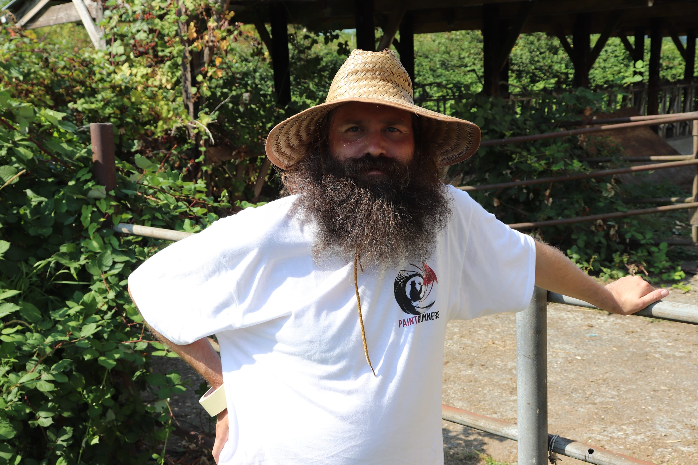 Bearded Paint Gunners painter in a straw sun hat standing at the edge of a job site
