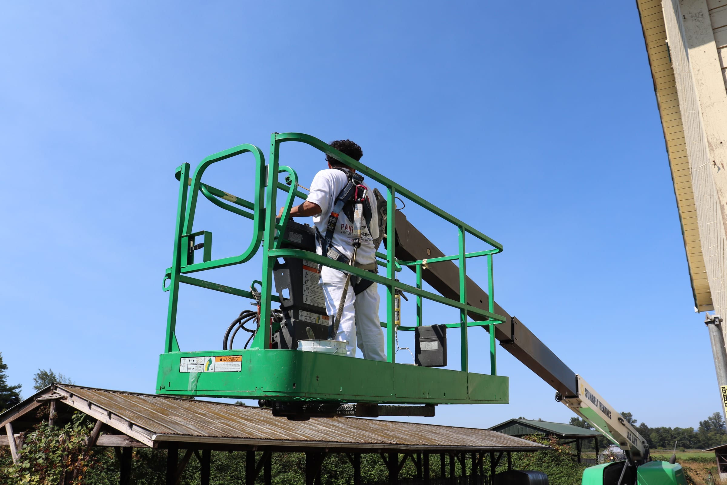 Paint Gunners painter working from the basket of a boom lift on a tall exterior wall