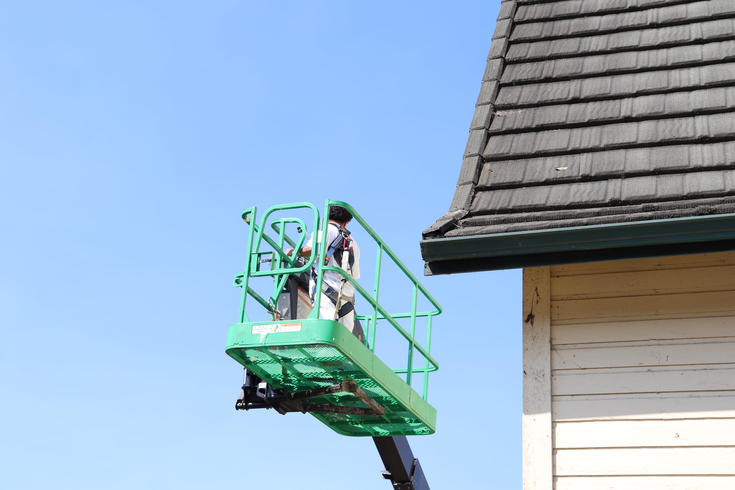 Boom lift basket raised to the roofline of a tall building against a clear blue sky
