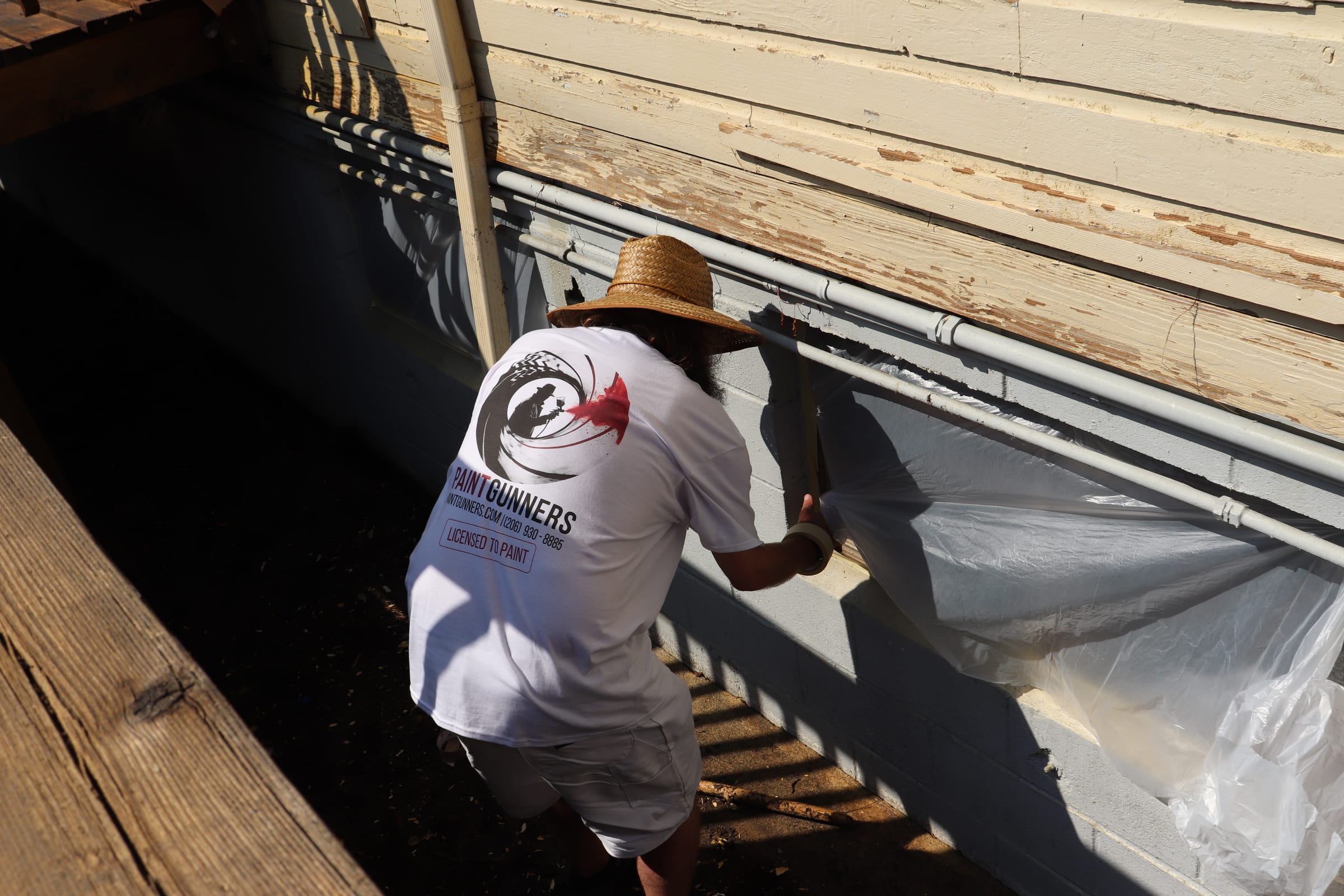 Painter masking sheeting along a roof edge before spraying the wall below