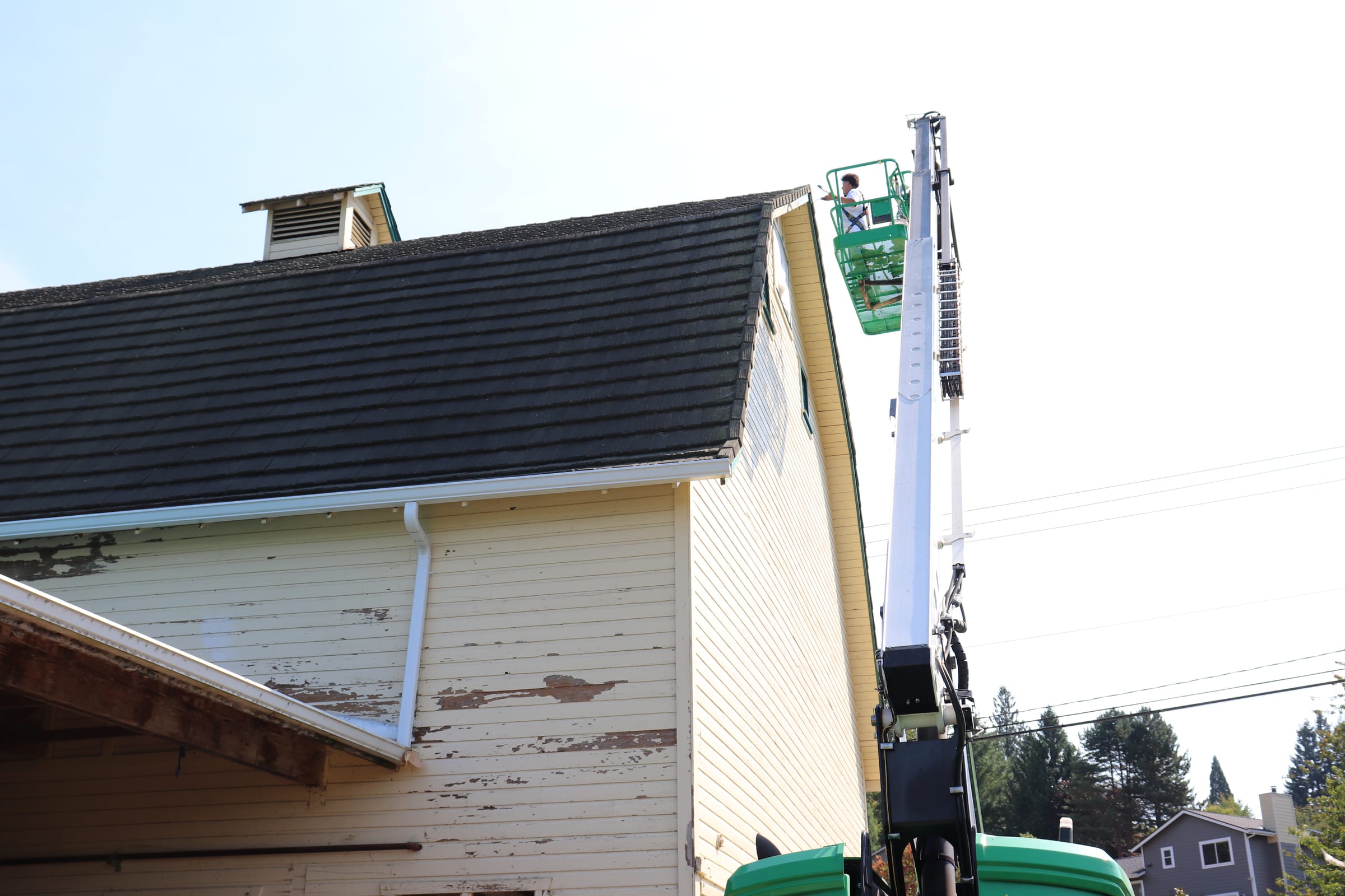 Badly peeling paint on the upper gable of a large barn with a boom lift staged below