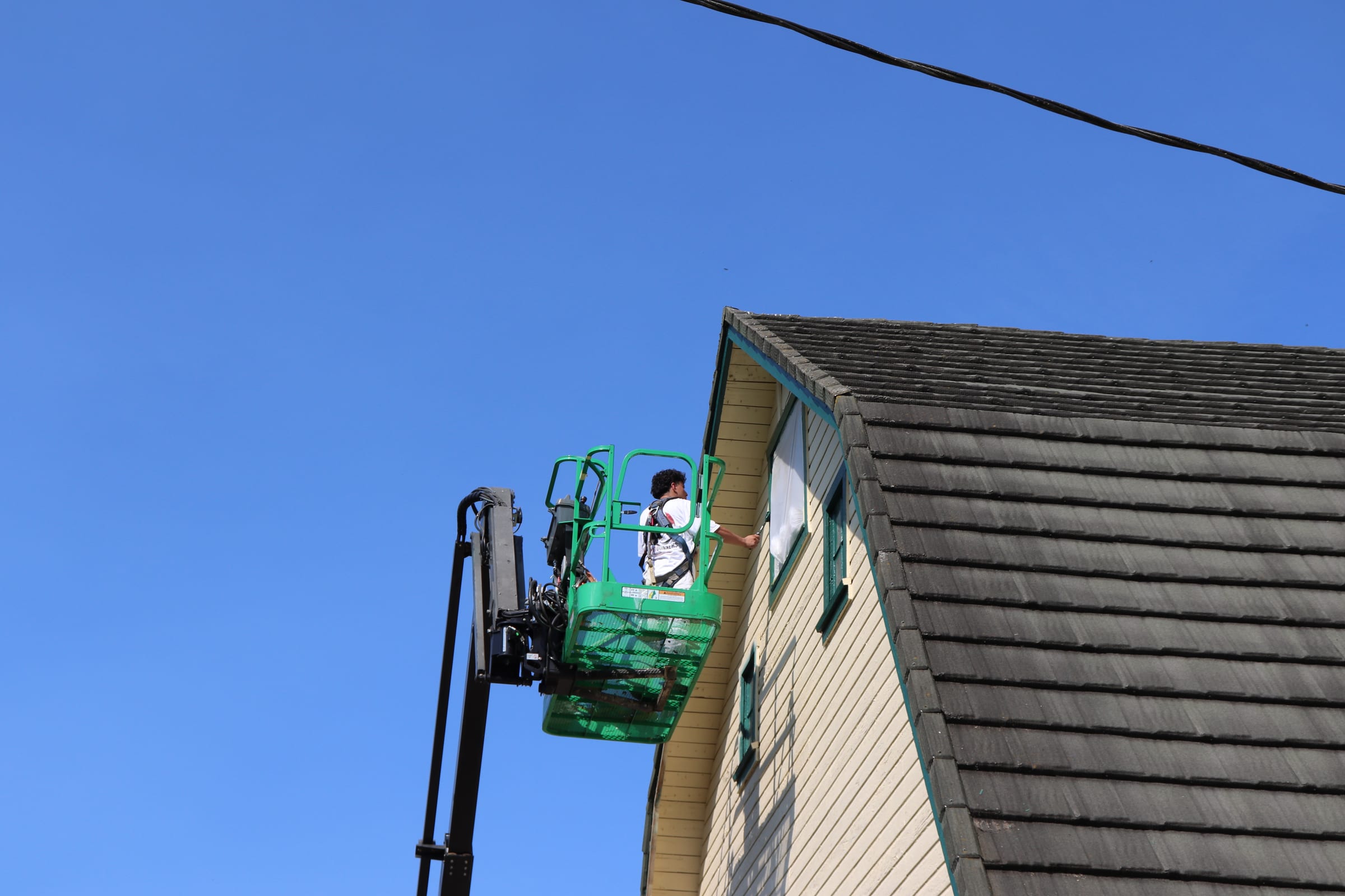 Painter in a boom lift working the gable end of a large barn under blue sky