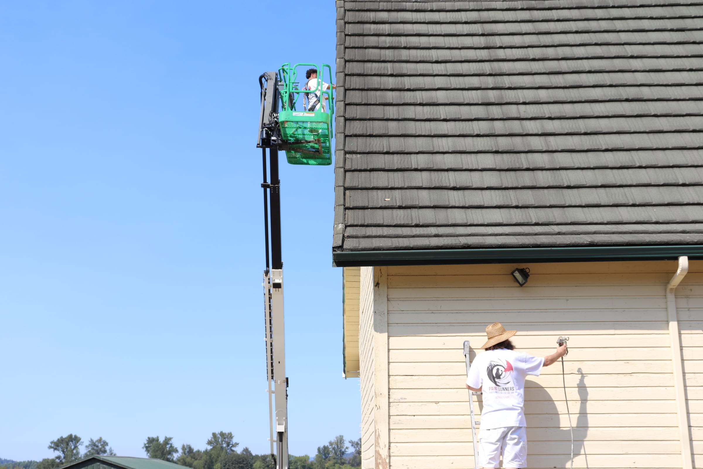 Painter spraying the lower section of a tall barn wall with the boom lift behind