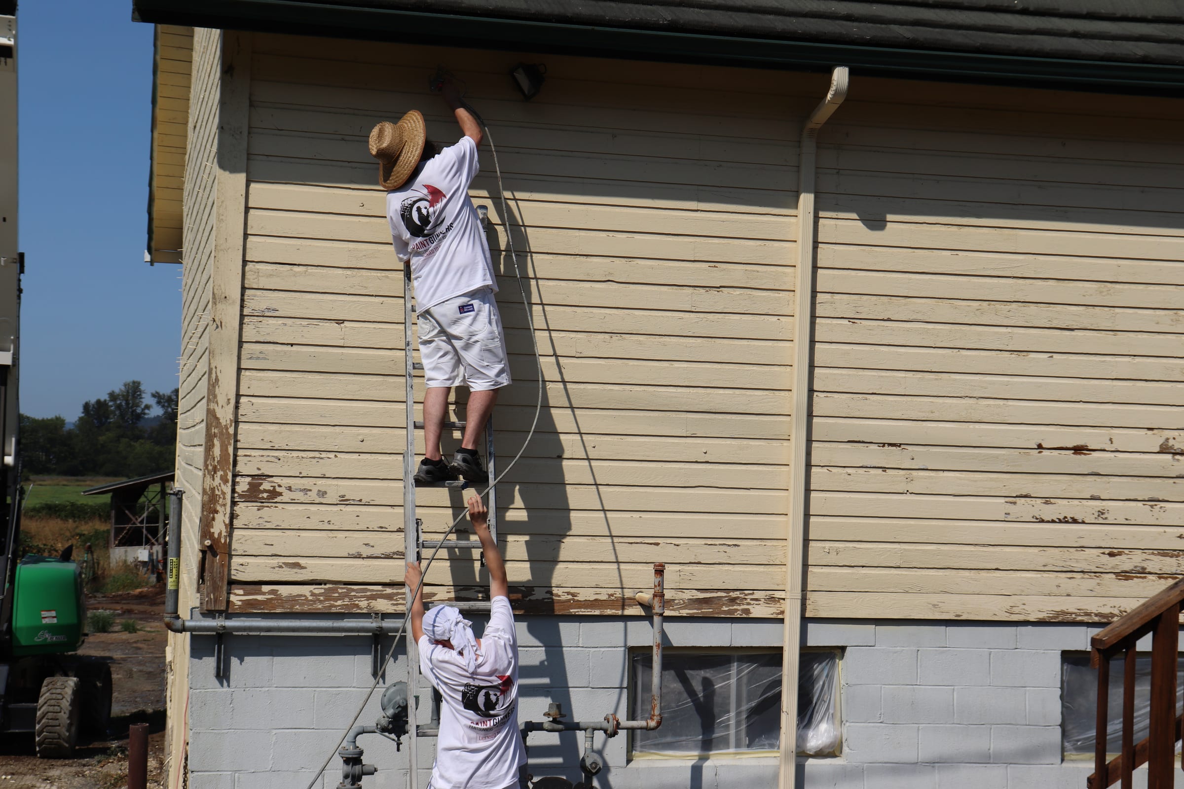 One painter working from a ladder while a second steadies it from below