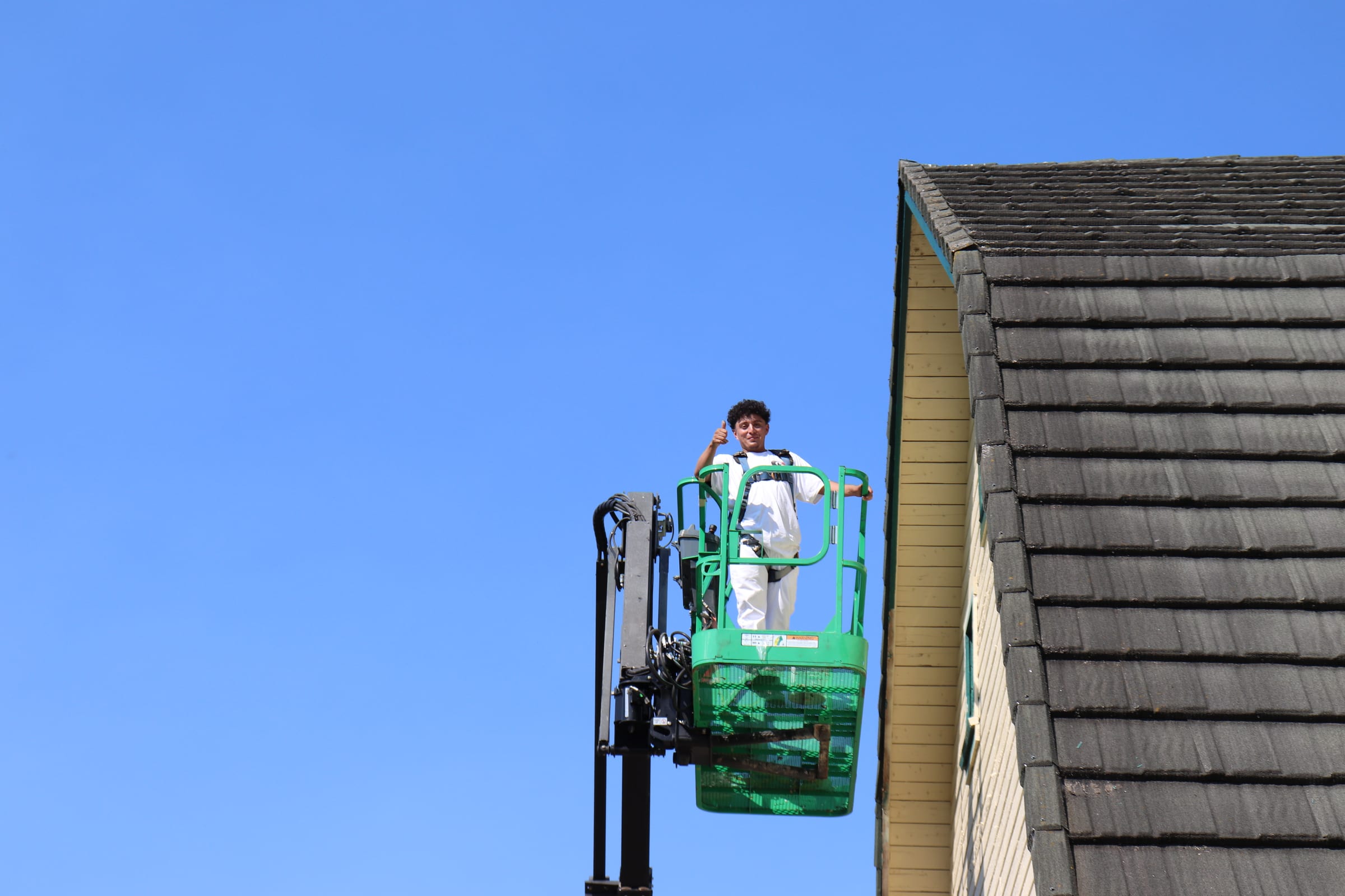 Painter standing in a raised boom lift basket against an empty blue sky