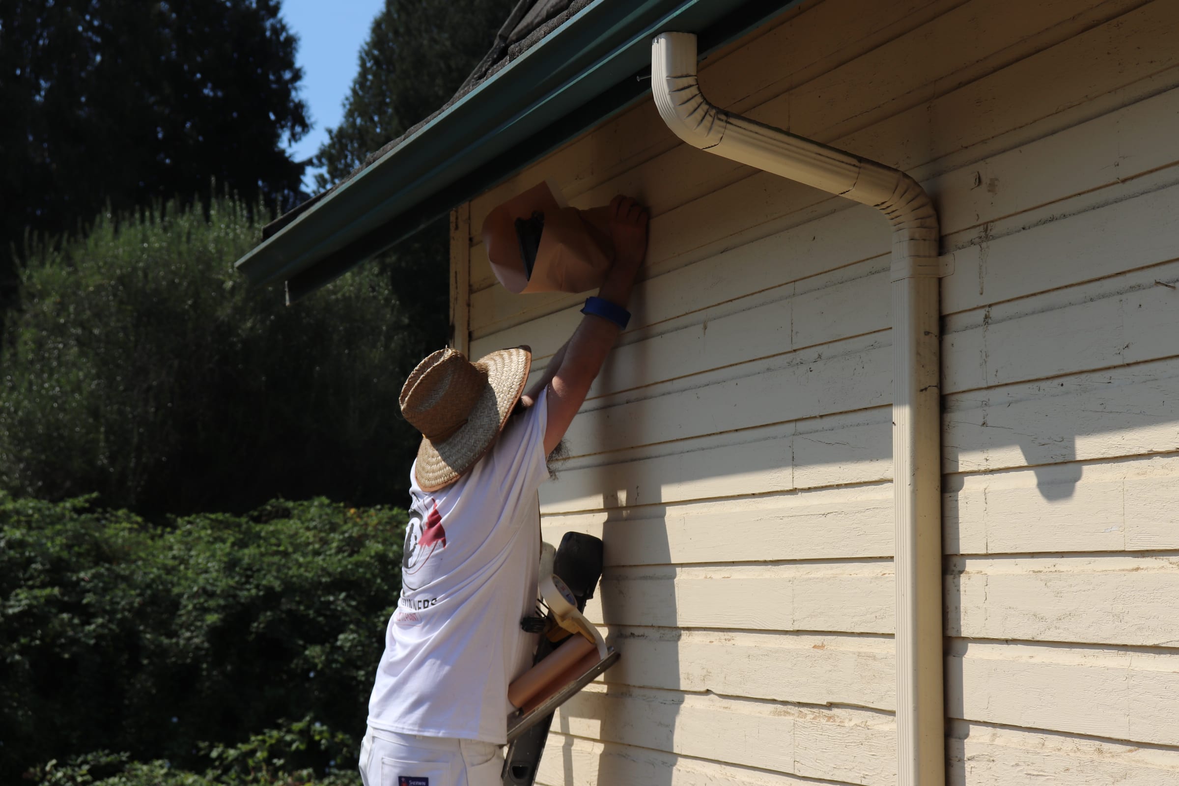 Painter reaching up under a roof eave to work a hard-to-reach section of trim