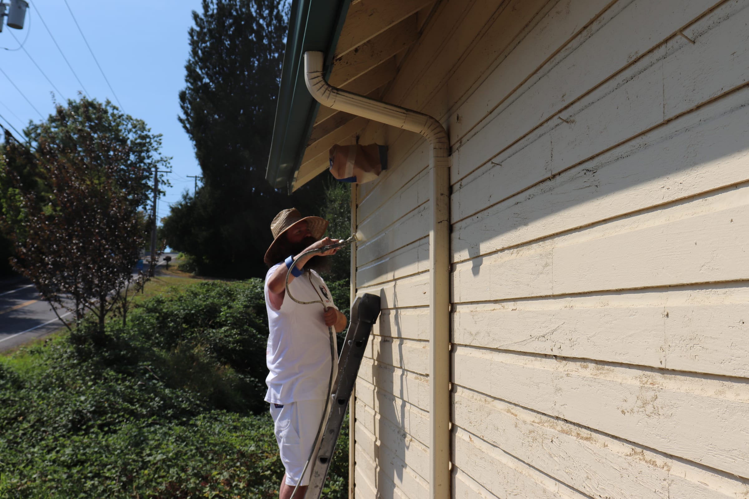 Painter holding an airless spray gun beside a freshly coated exterior wall