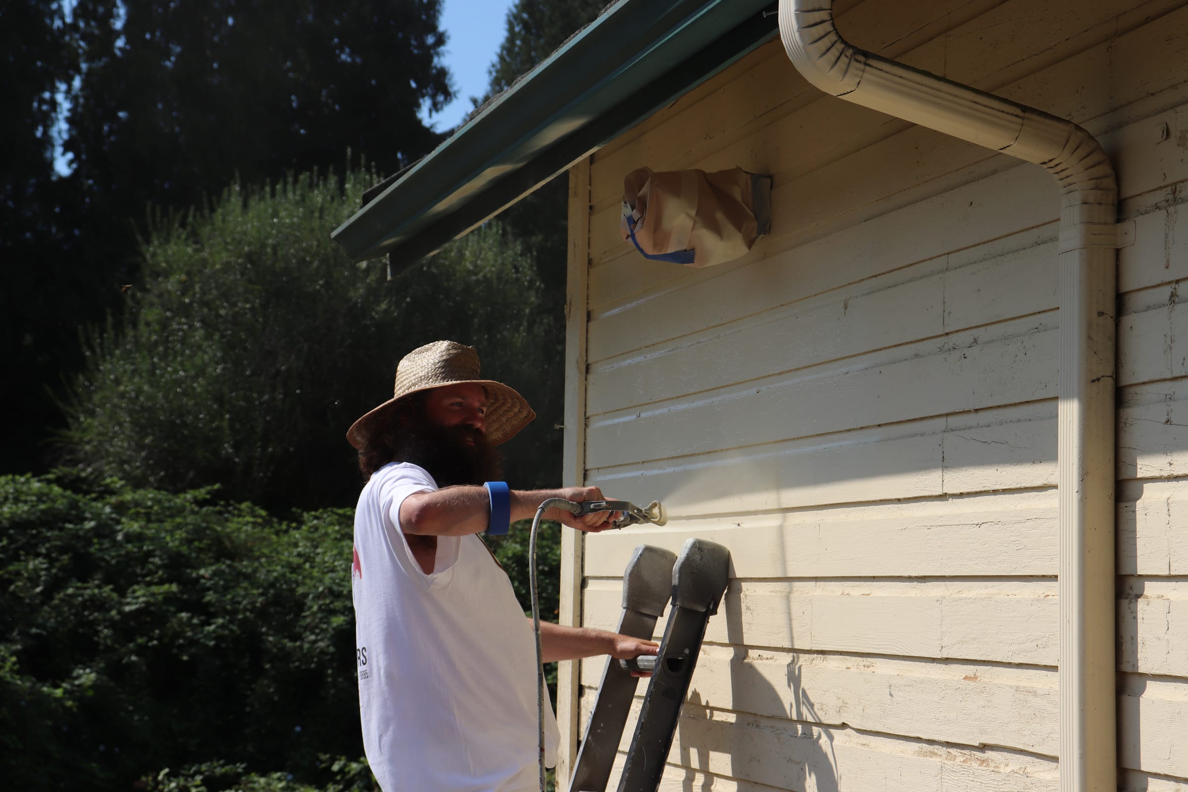 Airless sprayer laying a fresh coat across lap siding with visible spray mist