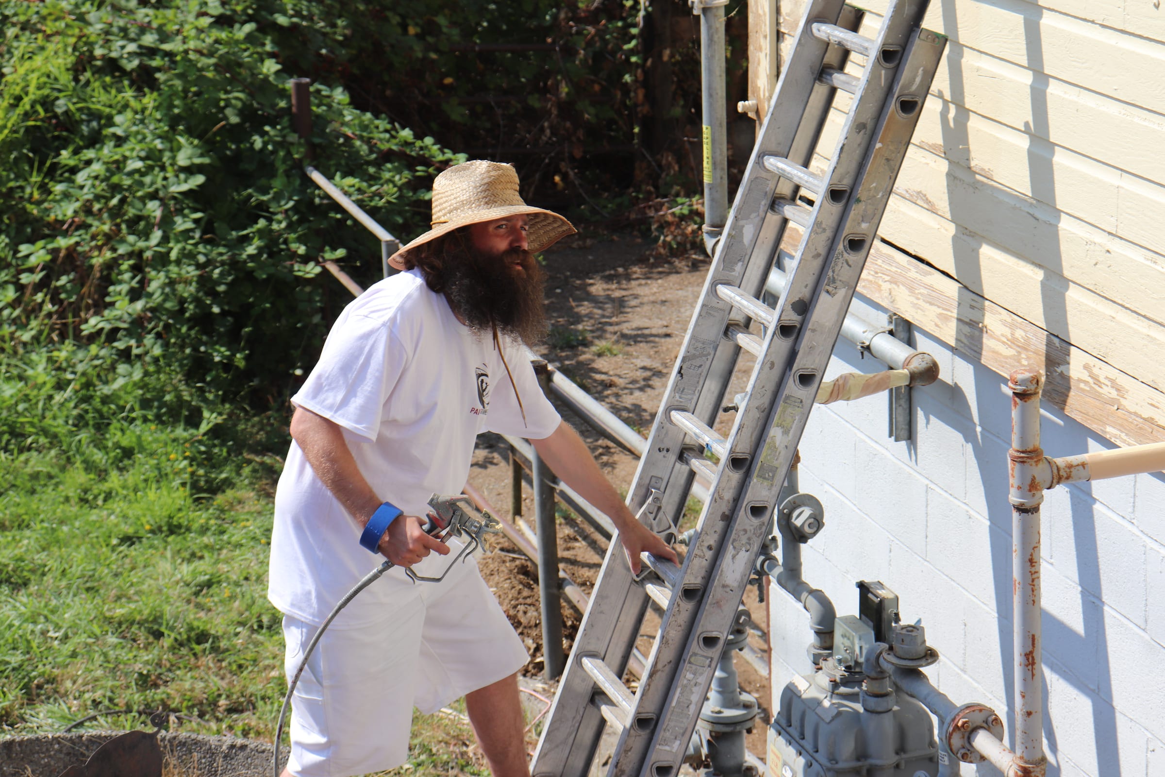 Painter with a spray gun beside a ladder and exterior gas piping