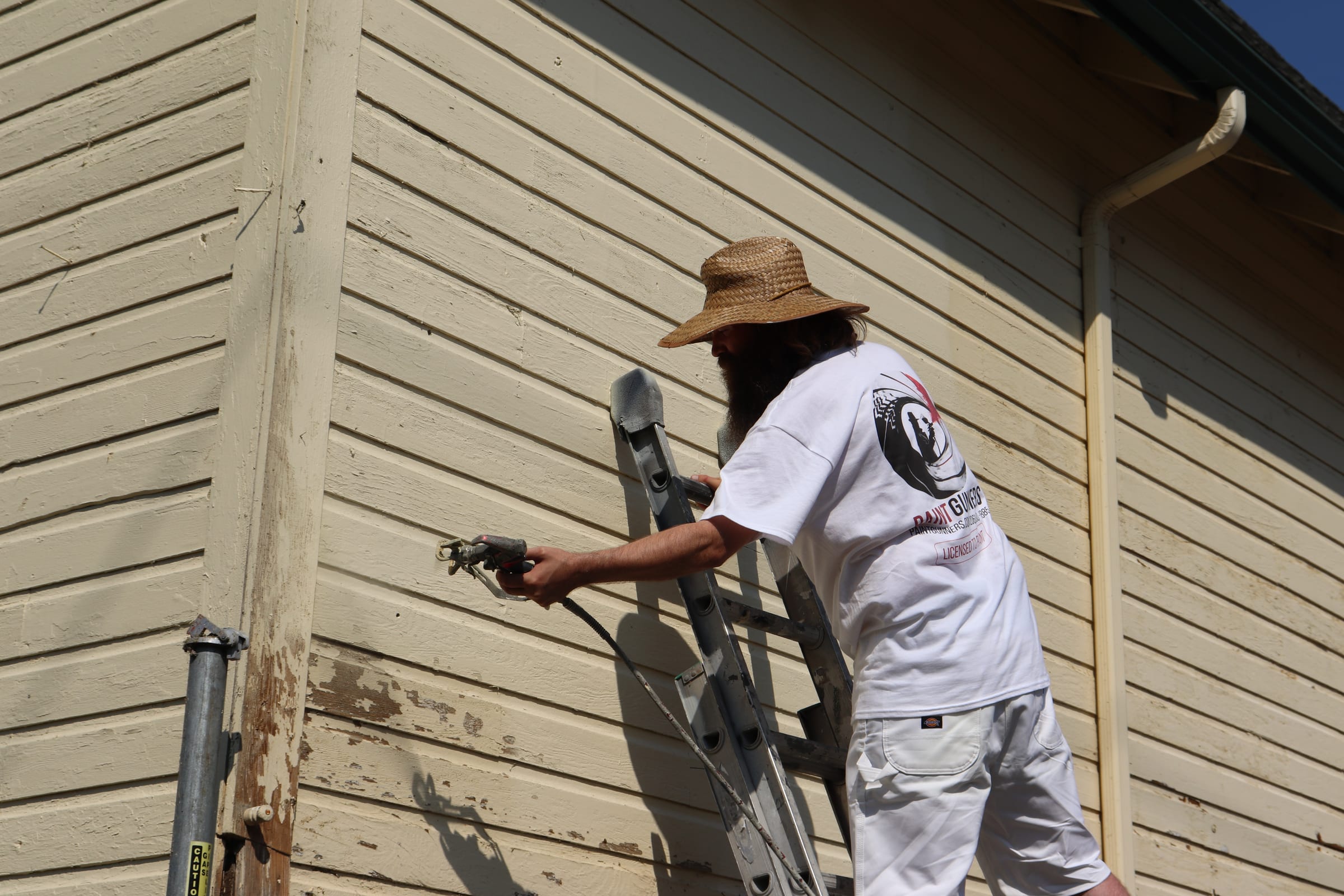Painter spraying paint into the corner board junction of an exterior wall