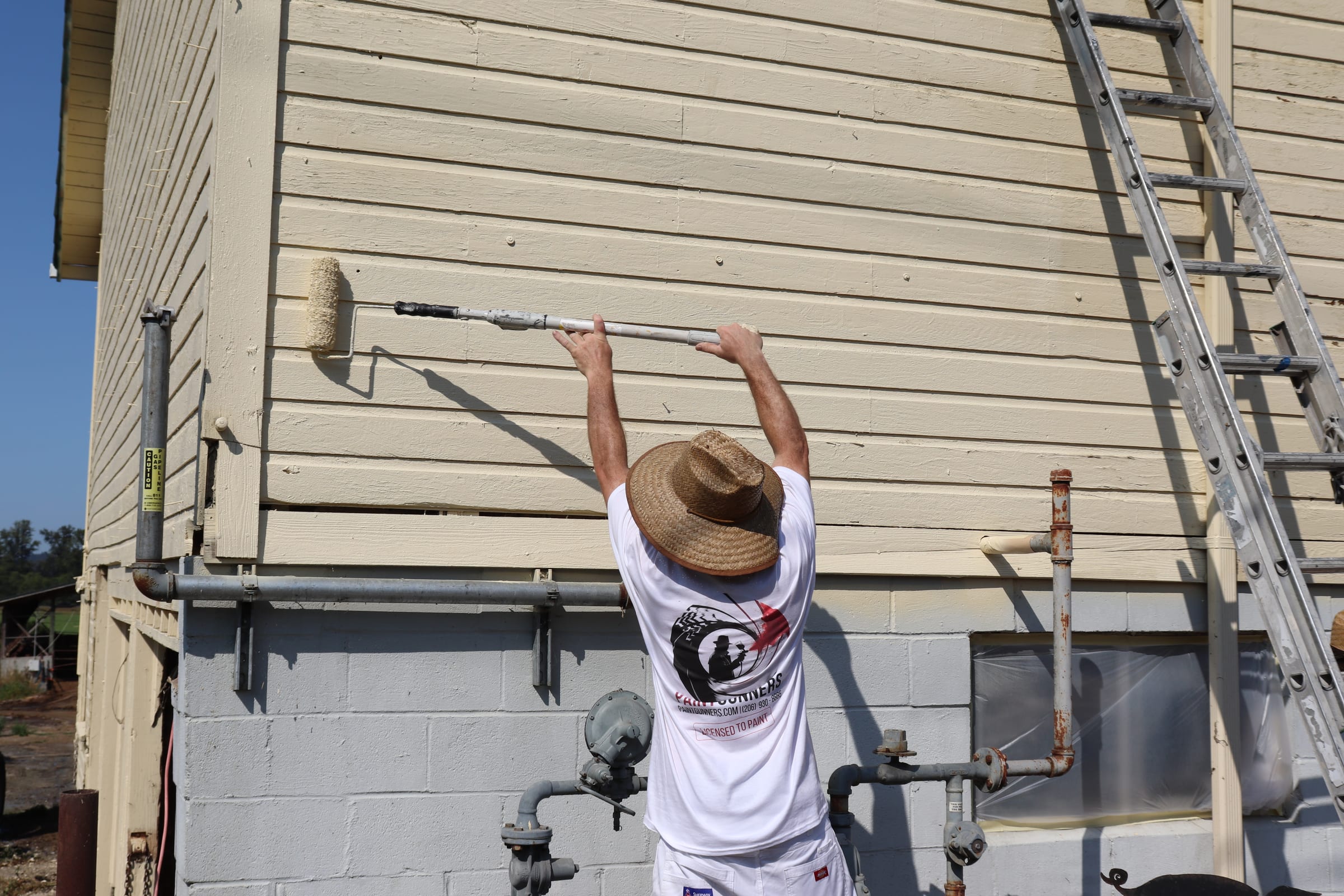 Painter using a roller on an extension pole to coat siding above a loading platform