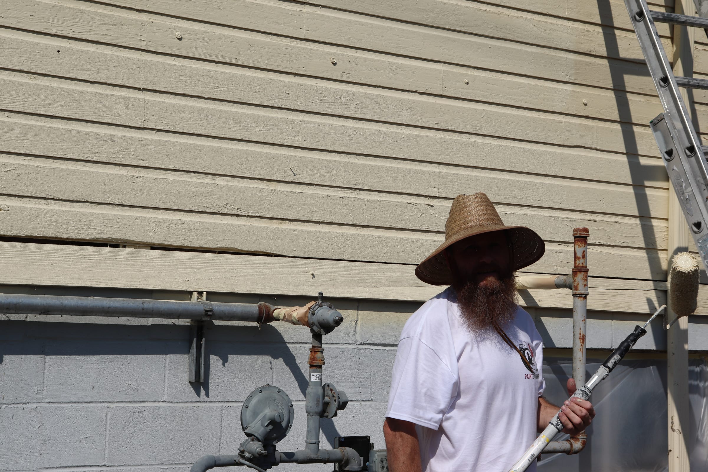 Painter carrying a roller pole beside exterior gas piping on a block wall