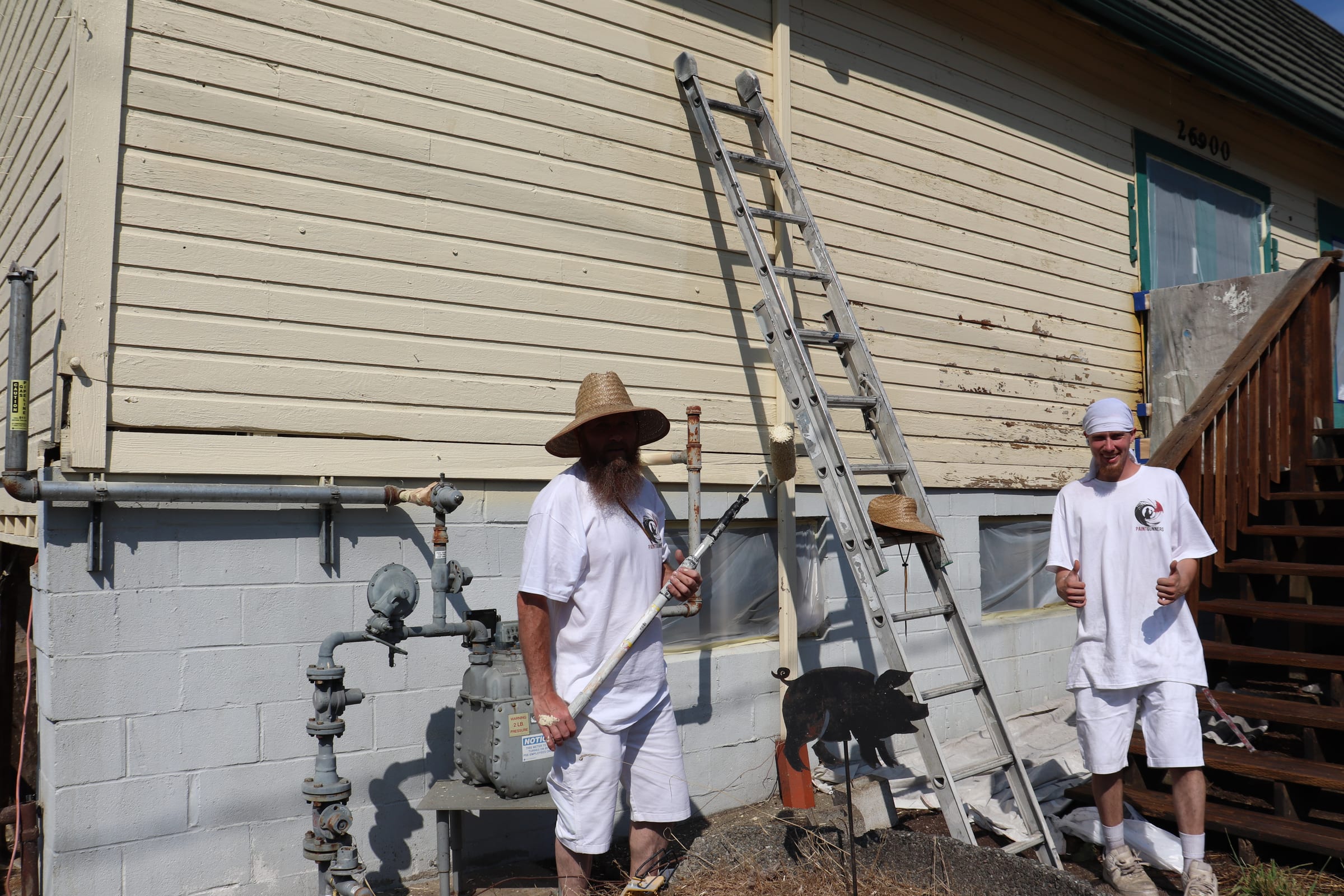 Two Paint Gunners crew members with roller poles working along a long exterior wall