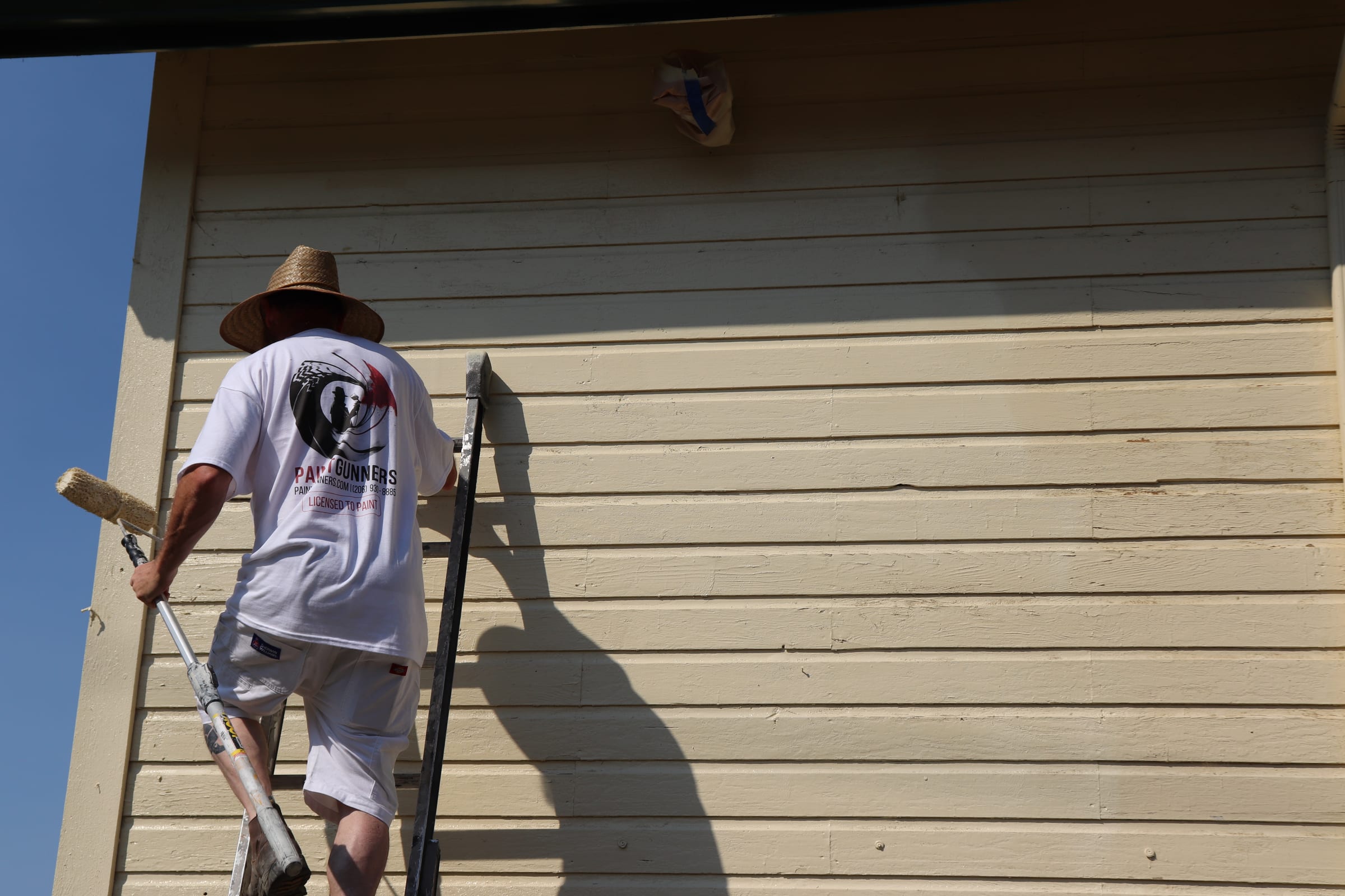 Low angle view of a painter on a ladder rolling paint onto upper siding