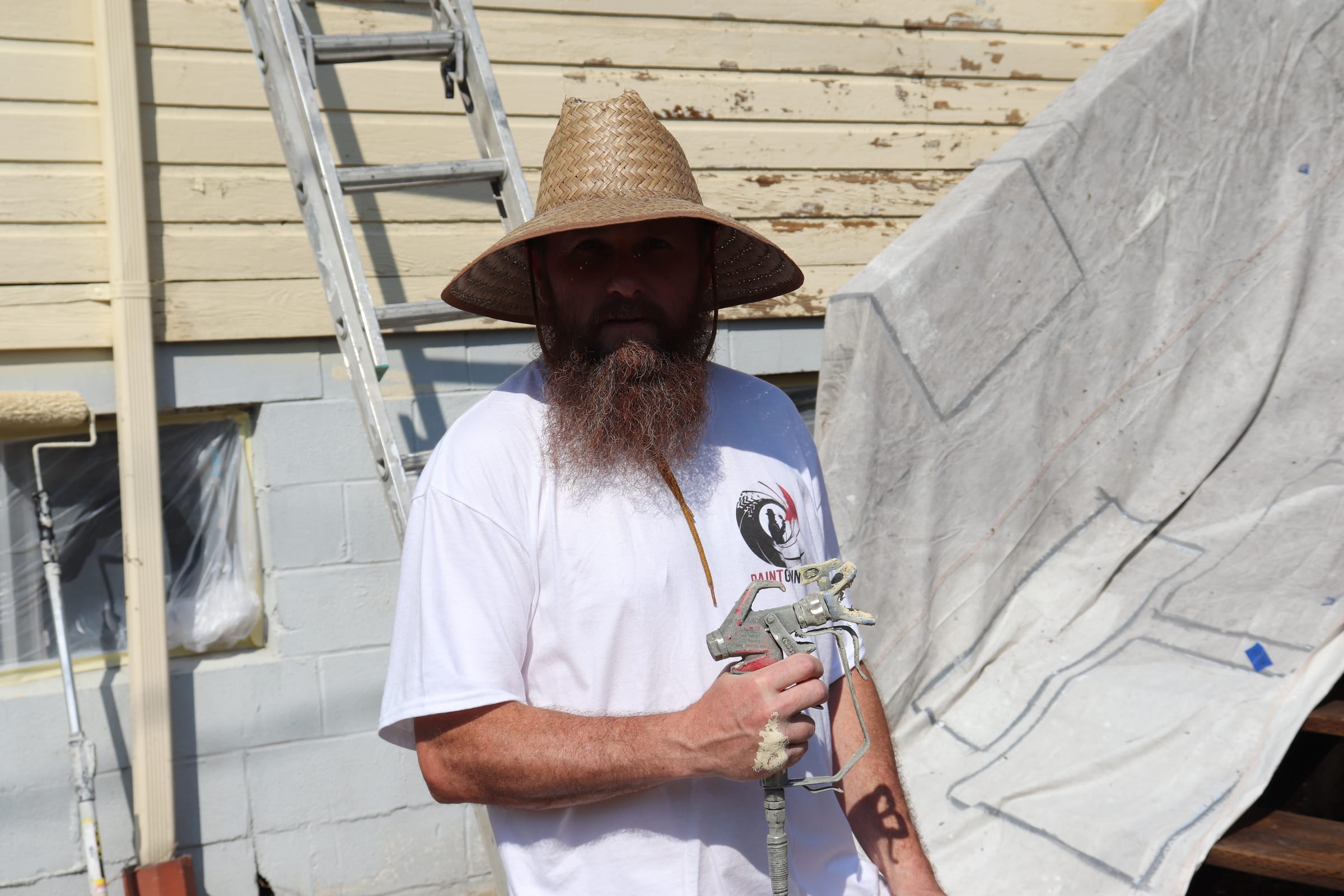 Bearded Paint Gunners painter holding an airless spray gun at a job site