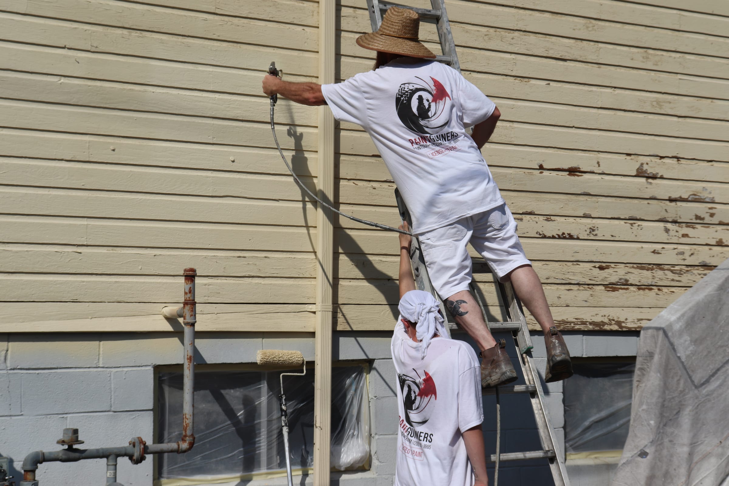 Painter spraying from a ladder while a colleague works at ground level below