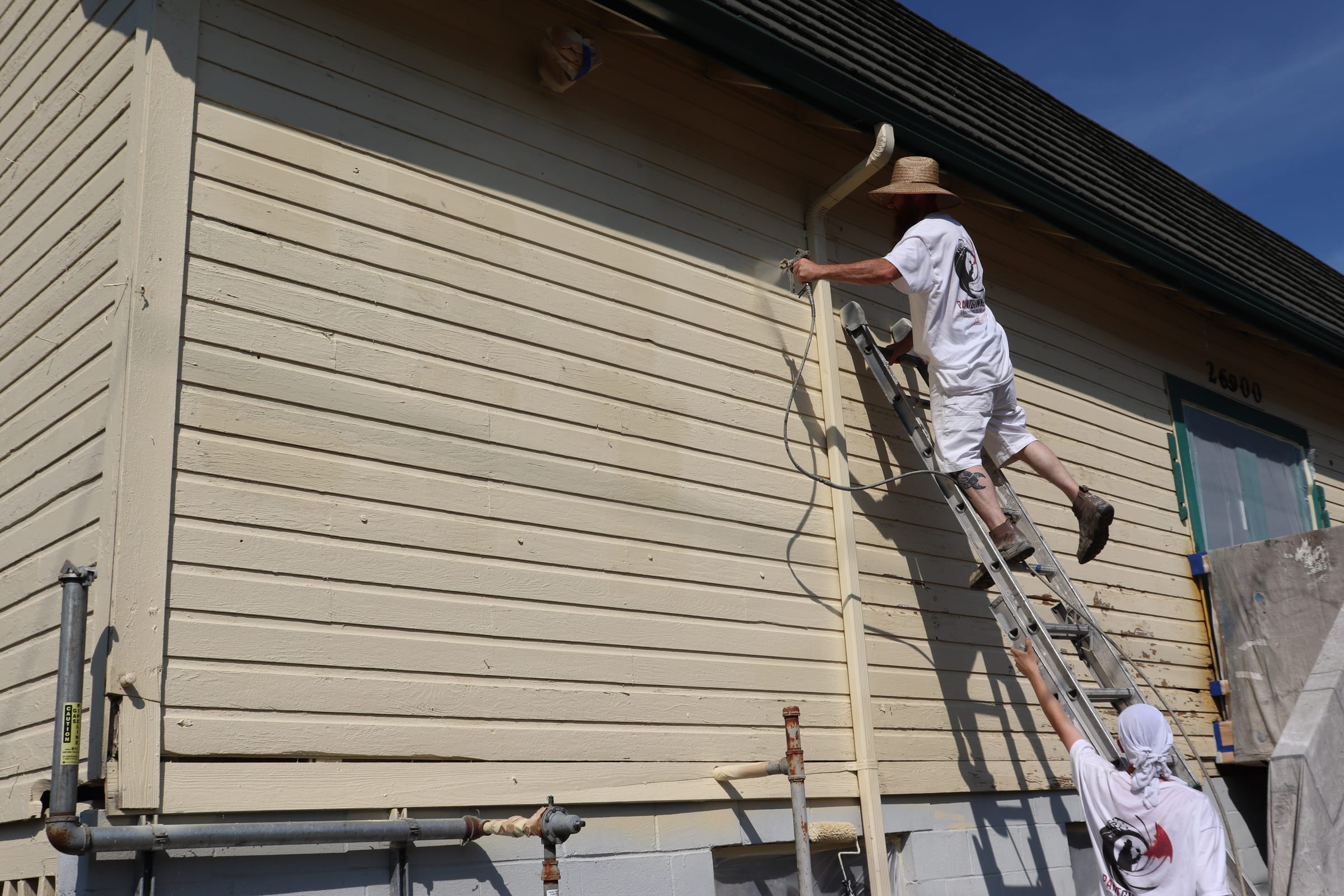 Painter climbing a ladder carrying an airless spray line up an exterior wall