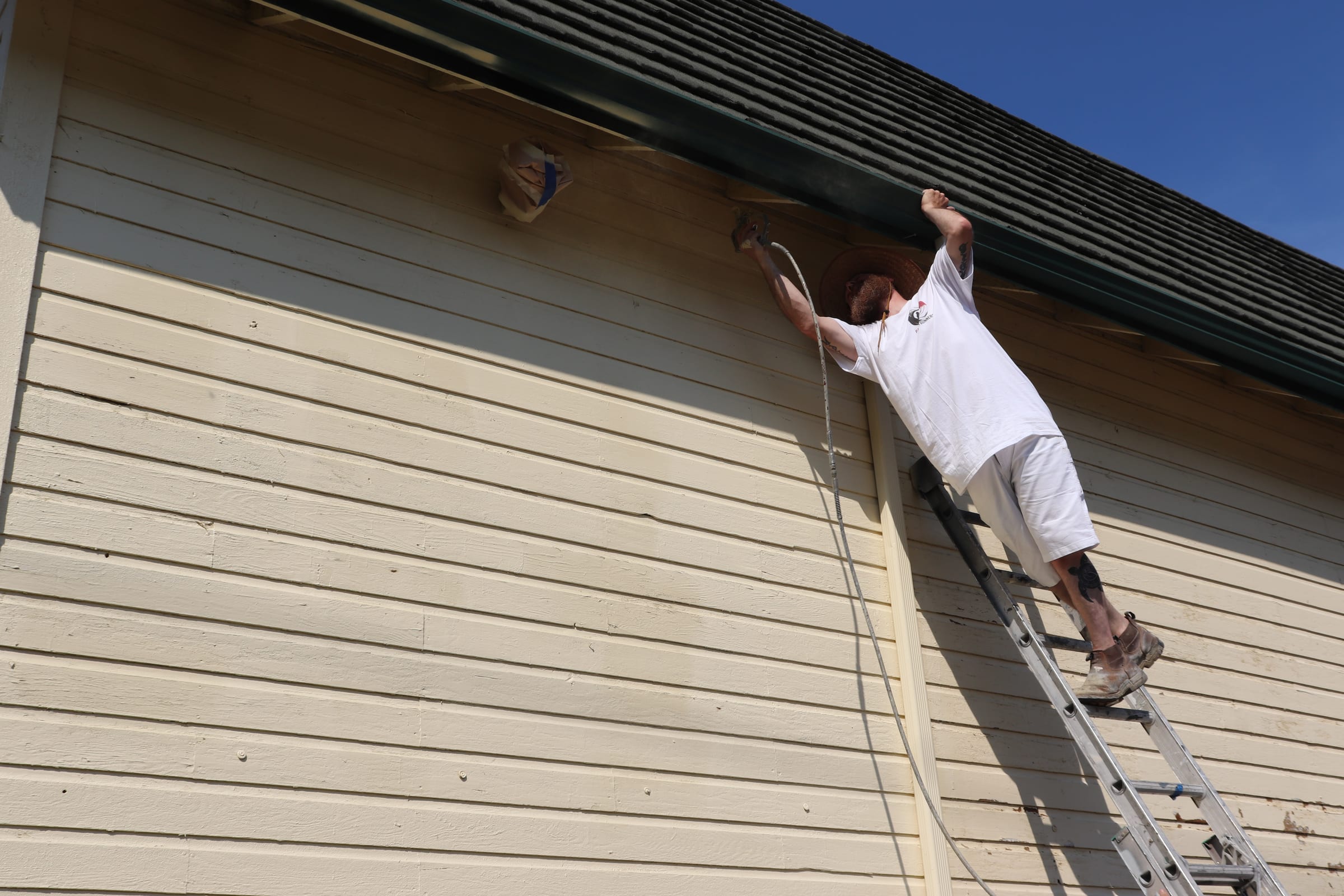 Painter reaching the eave line from high on an extension ladder
