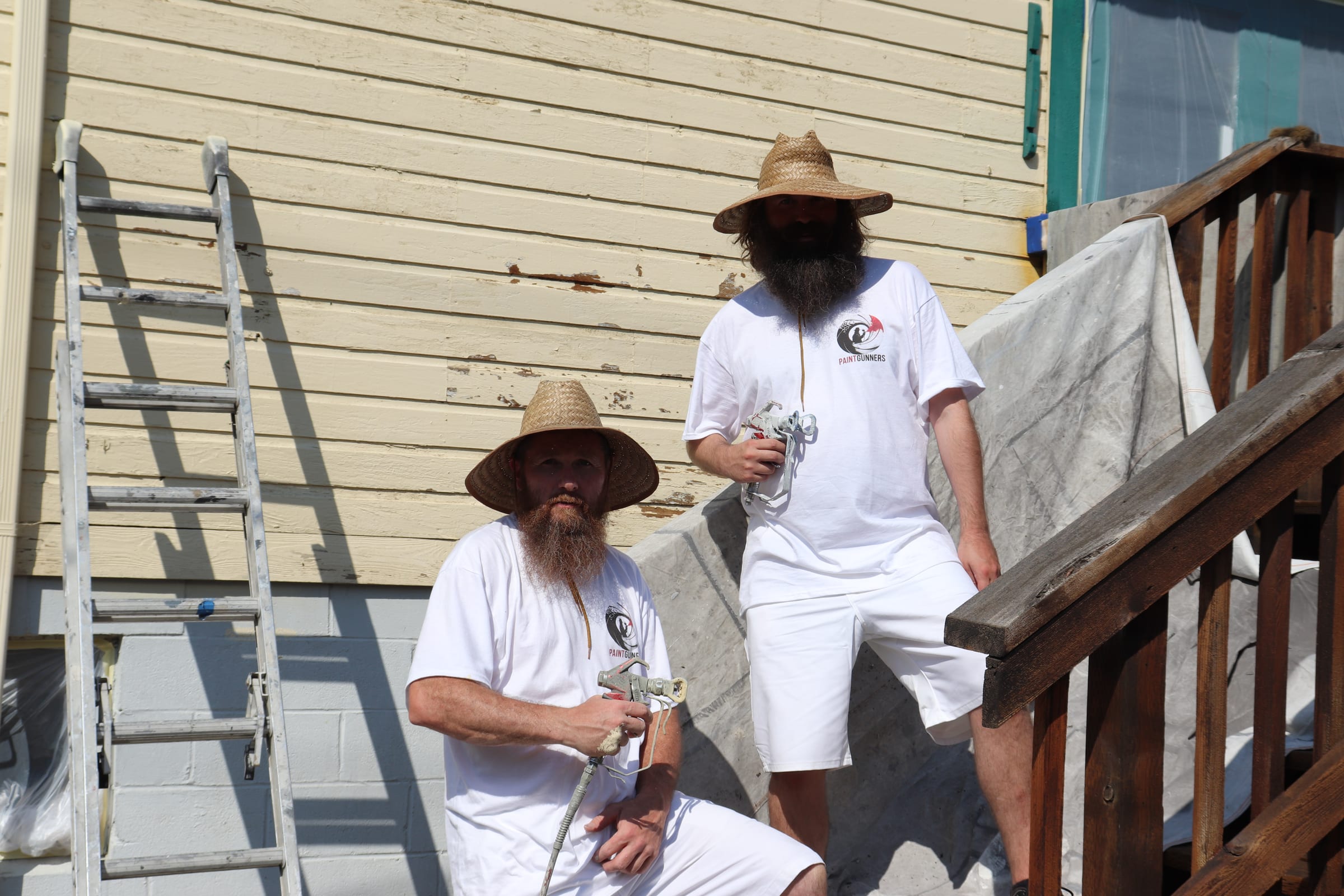 Two Paint Gunners painters standing with airless spray guns beside an exterior staircase