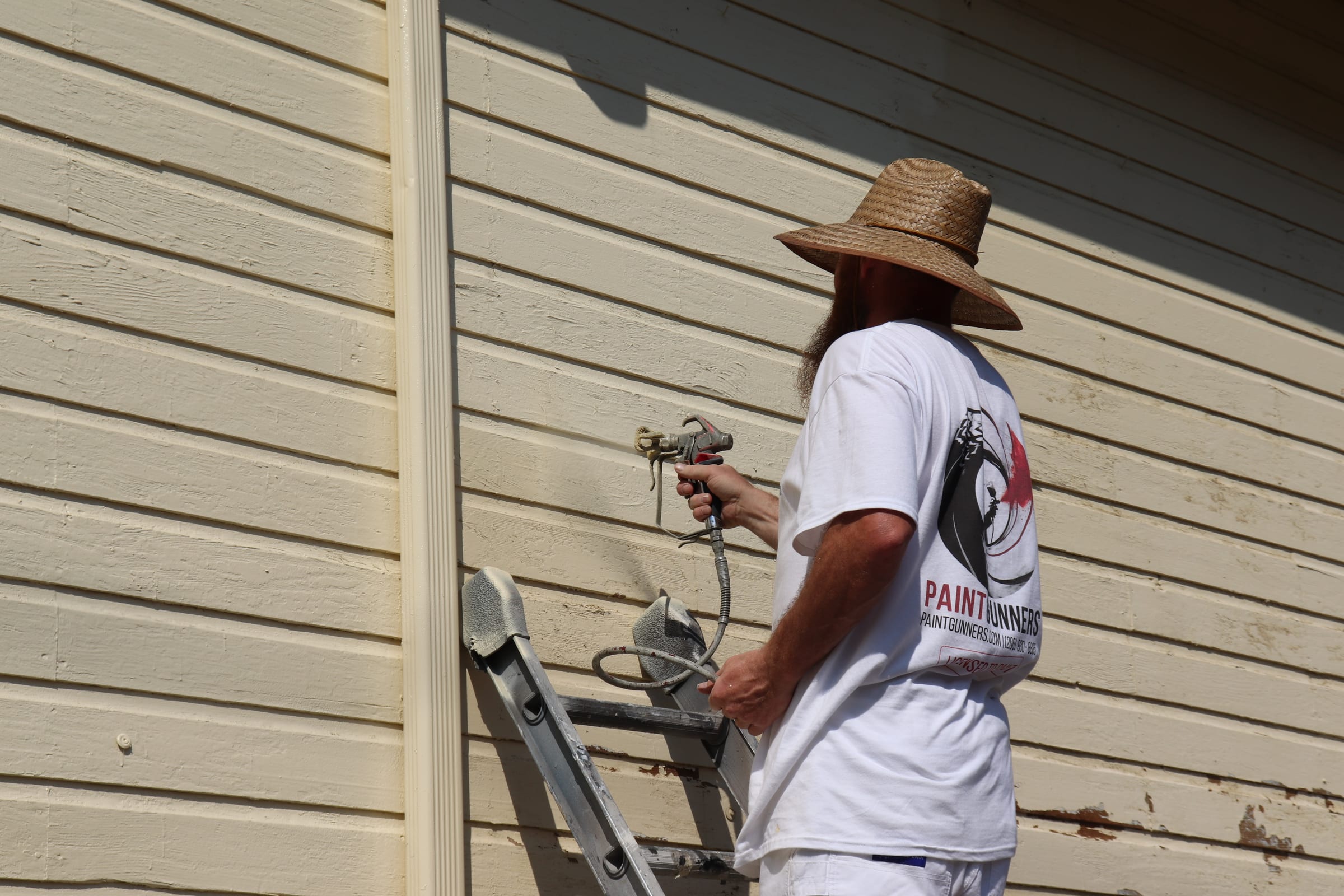 Painter making a side-on spray pass across horizontal siding