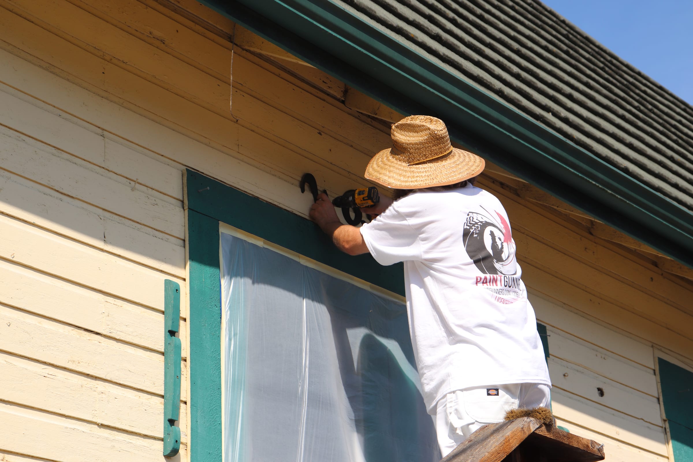 Painter working the edge of a teal window trim with the glass fully masked off