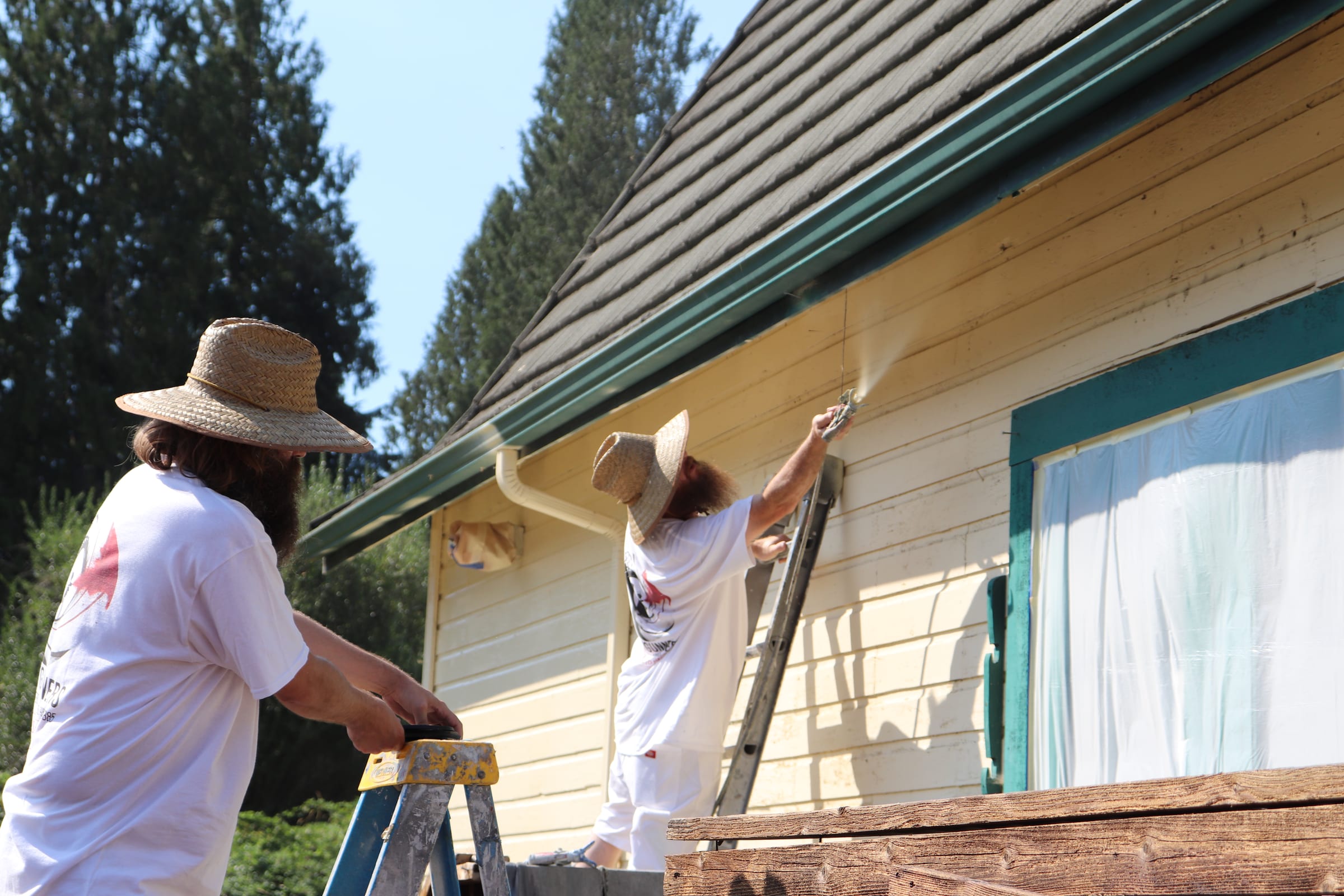 Two painters coating an eave, one working from a stepladder