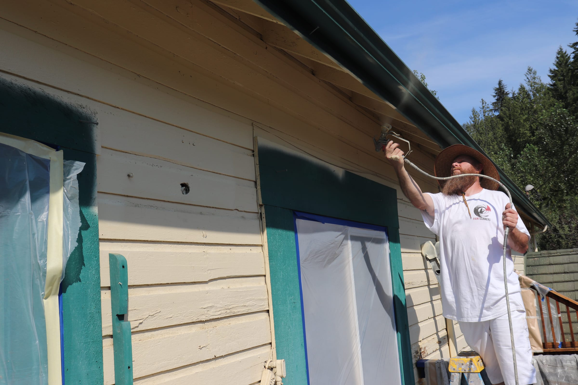 Painter spraying the underside of an eave from ground level