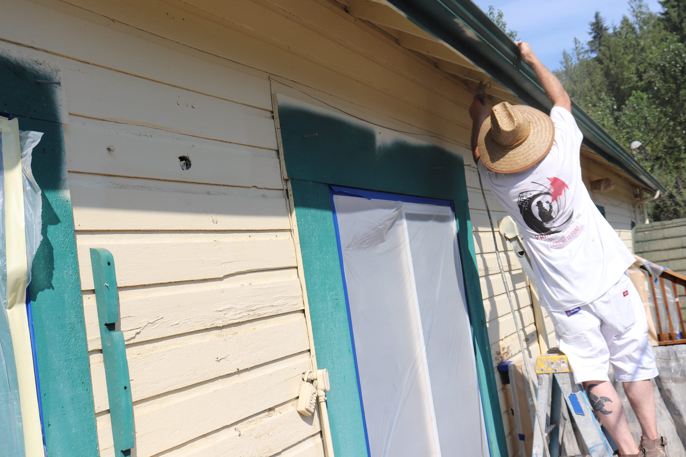 Painter reaching above a masked window to finish the trim line