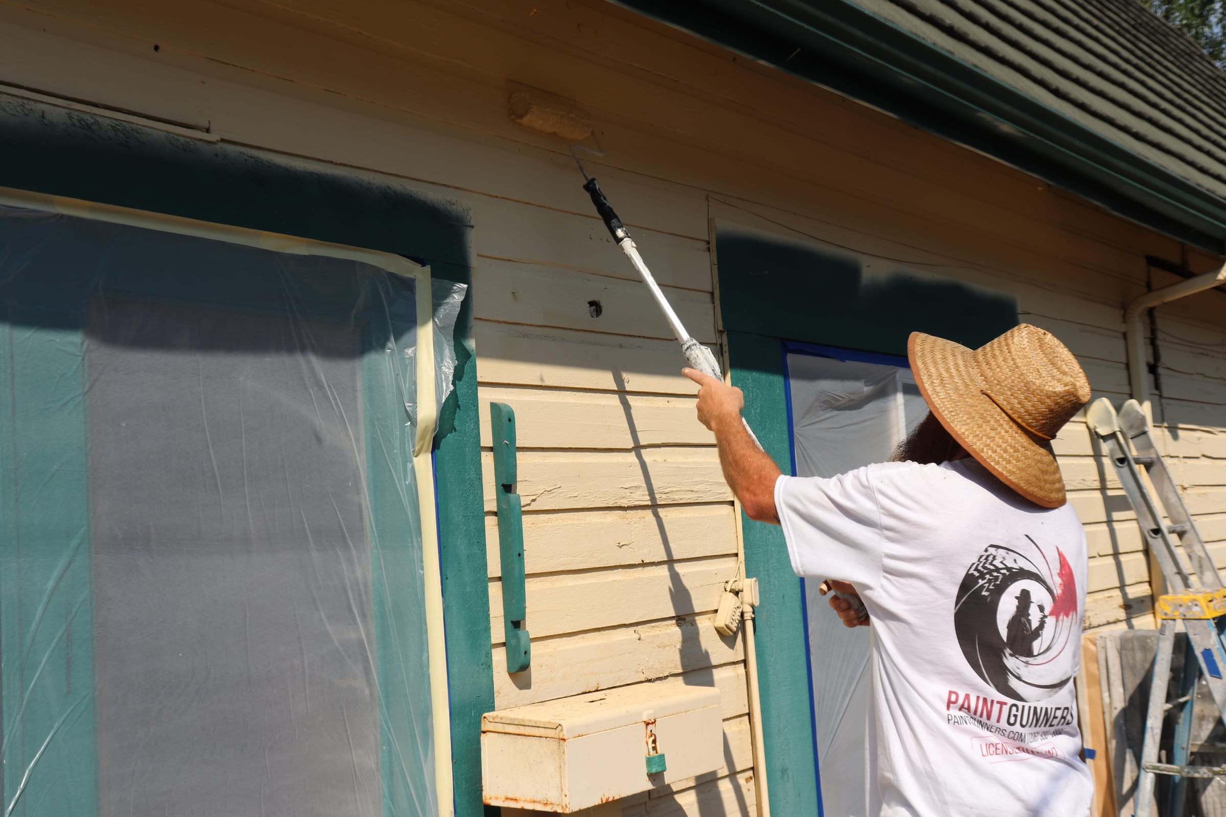 Painter using an extension pole roller alongside a masked window opening