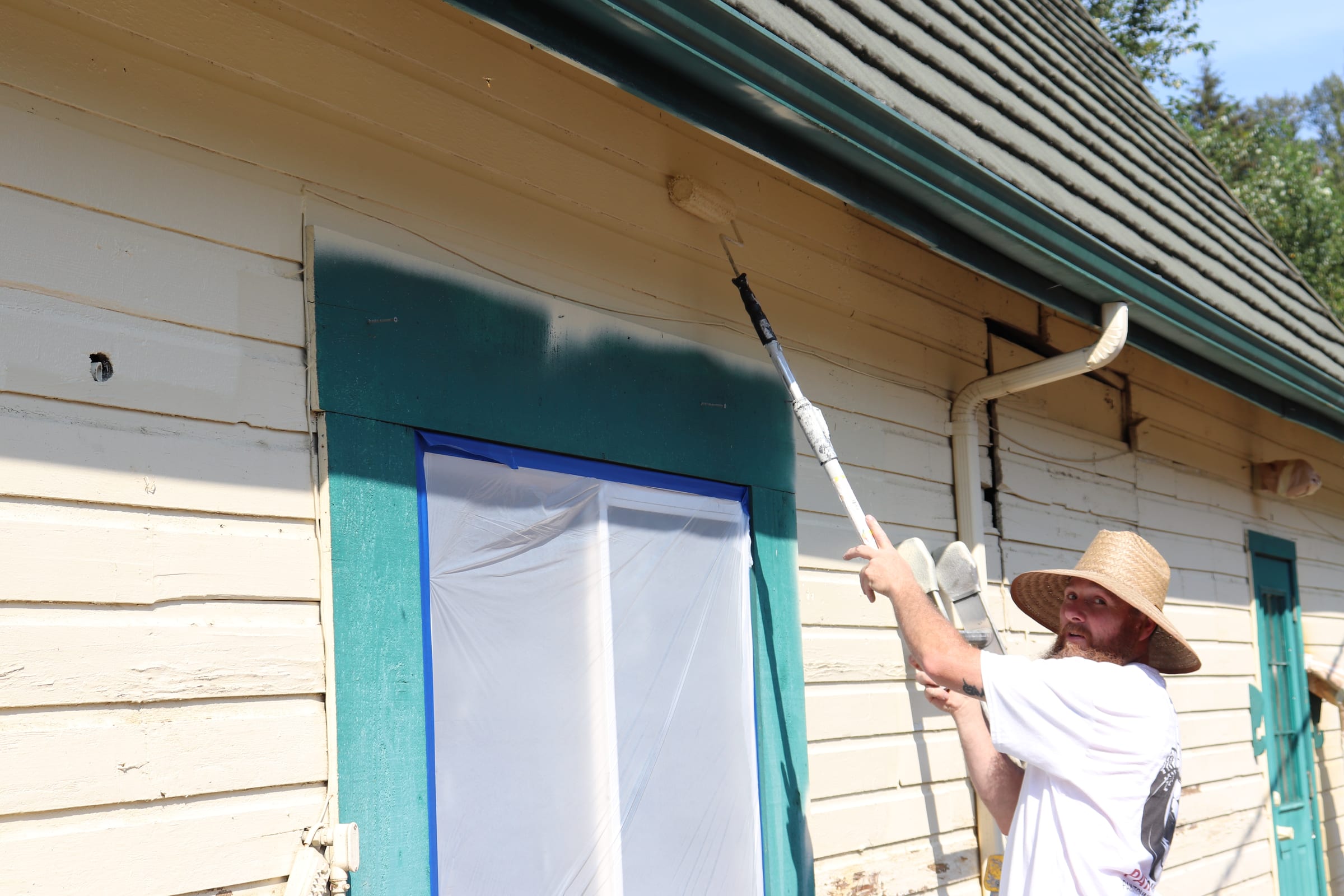 Painter rolling deep teal paint along a trim band using an extension pole