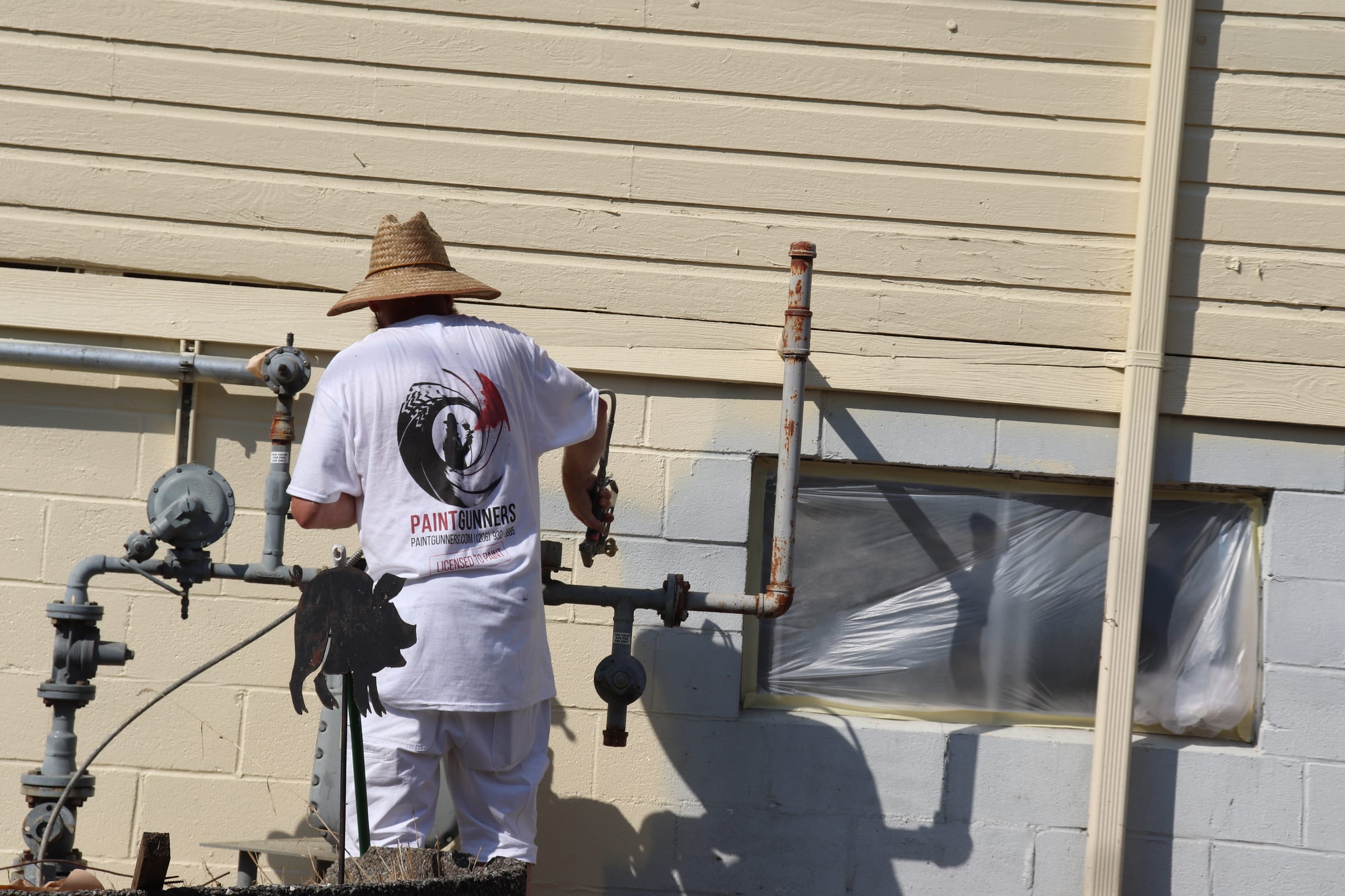 Painter coating a block wall behind exterior gas piping