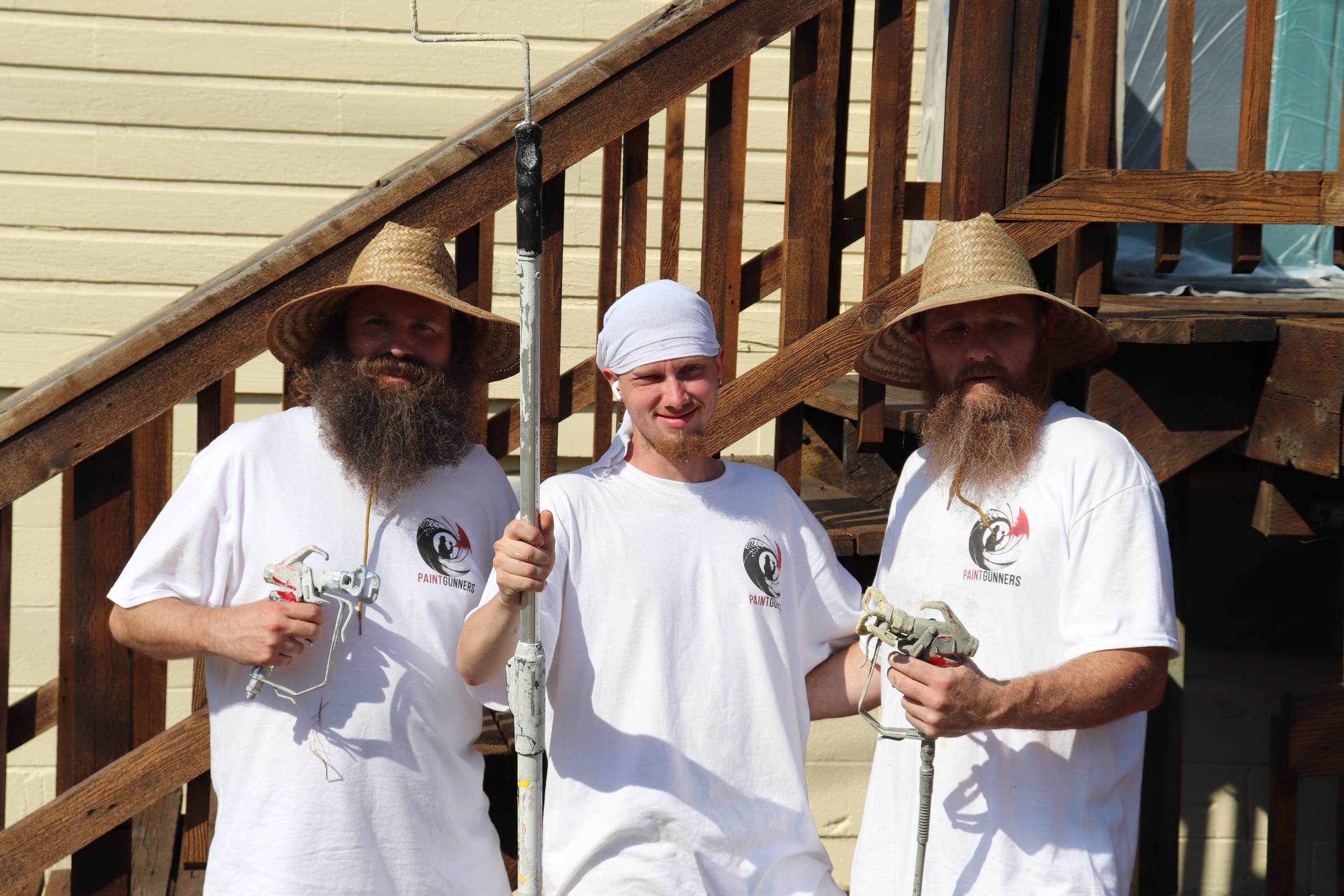 Three Paint Gunners crew members standing together with spray guns and a roller pole