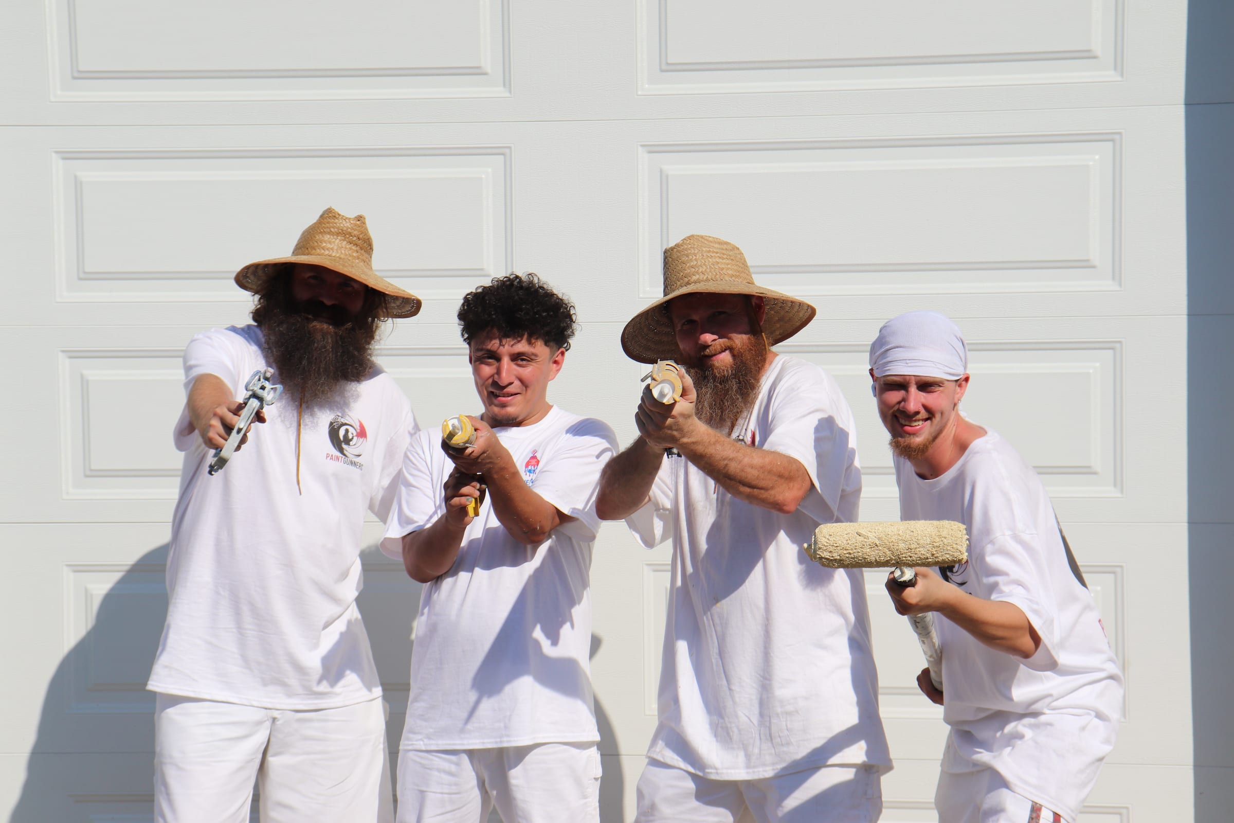 The Paint Gunners crew standing together with spray guns and a roller against a white door